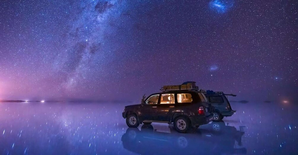 A dark-colored SUV parked on a reflective surface under a starry night sky with a visible Milky Way. 5