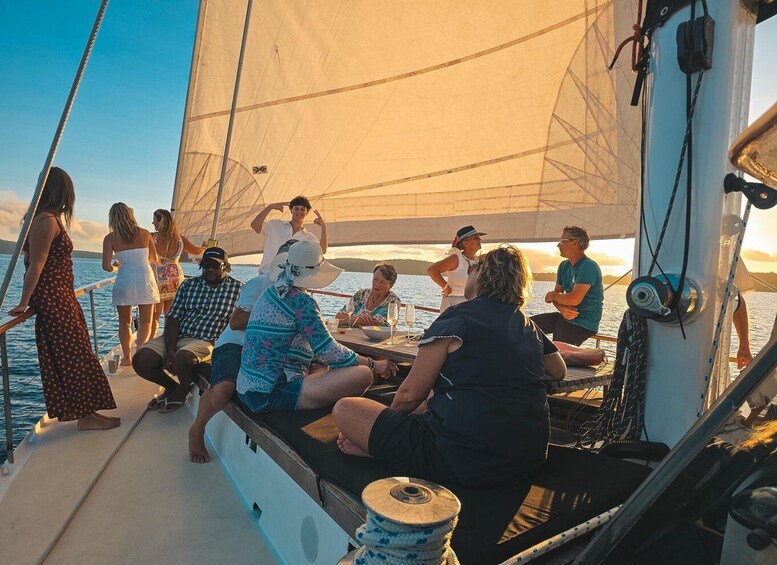 A group of people on a sailboat with a sail unfurled, enjoying a sunset. 4