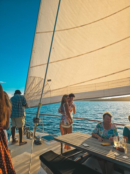 A sailboat with people on deck, a clear blue sky, and calm water. 3
