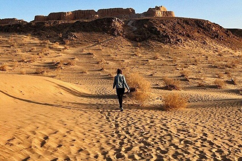 A person walking in a desert with sand dunes and rocky formations in the background. 3