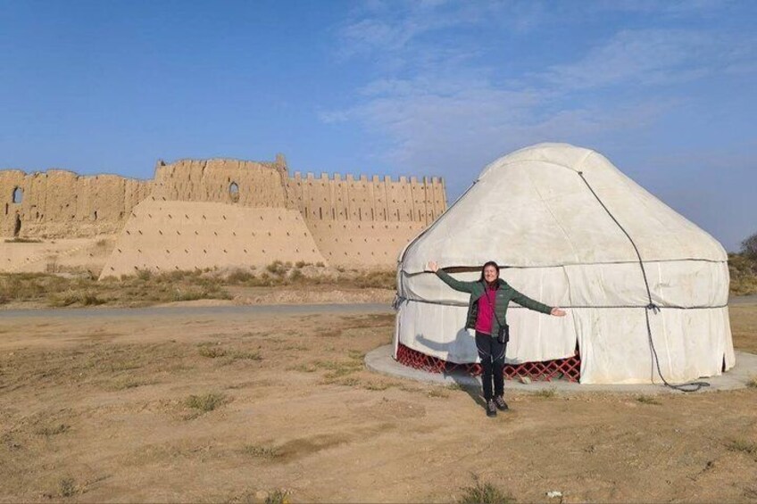 A person standing in front of a traditional yurt with a large fort in the background. 4