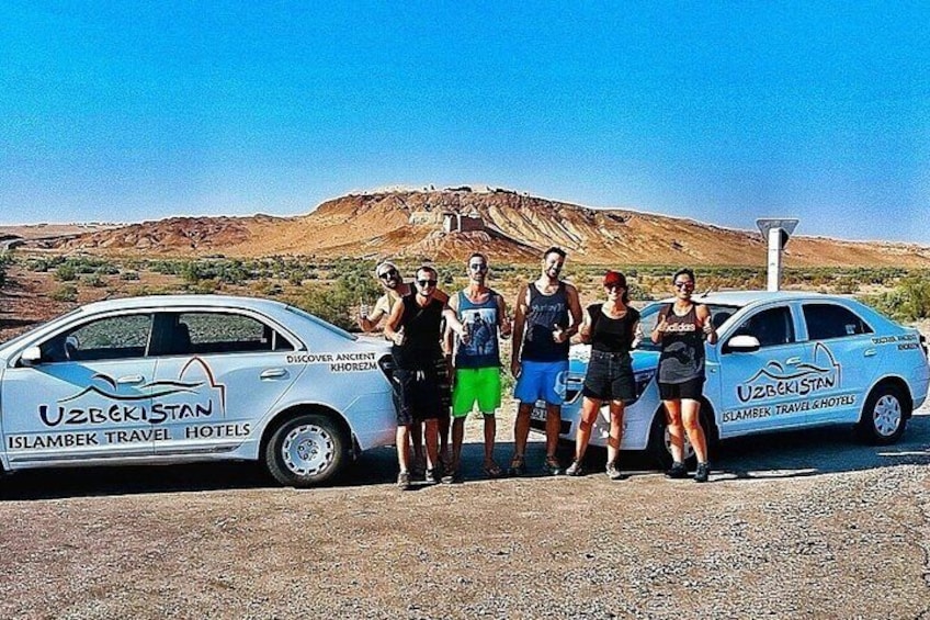 A group of people standing next to two cars with 'Uzbekistan' and 'Islambek Travel Hotels' logos. 1