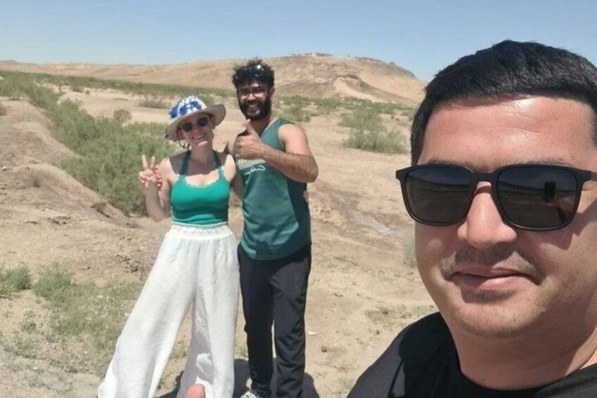 Two people in a desert landscape with sparse vegetation and hills in the background. 5