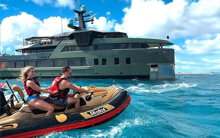 A jet ski with two people wearing life jackets, a large military ship in the background, and clear blue skies. 5