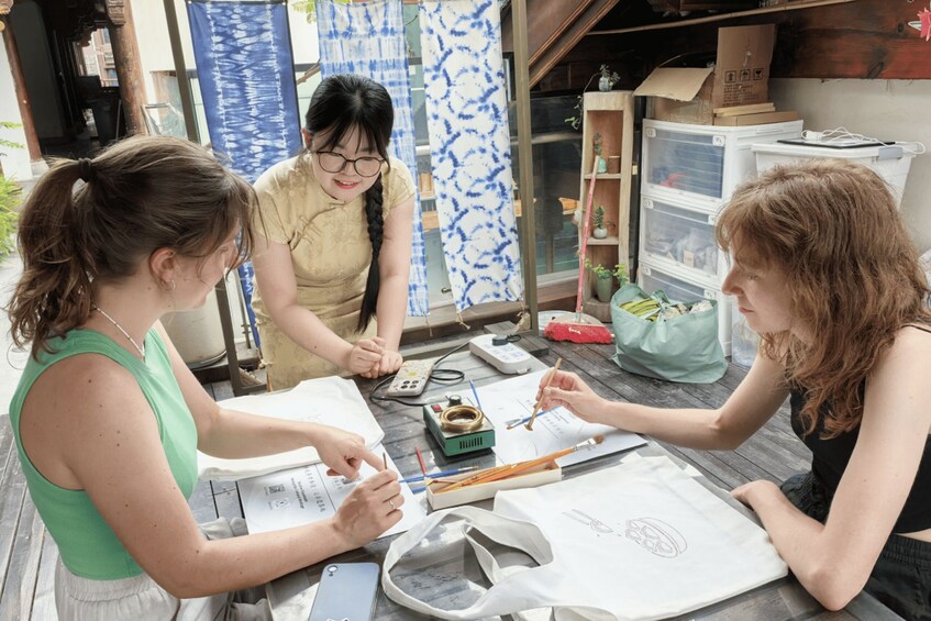 Three people engaged in a drawing activity at a wooden table with art supplies. 3