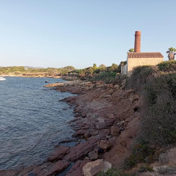 A coastal landscape with a rocky shoreline, a building with a chimney, and a boat in the water. 3