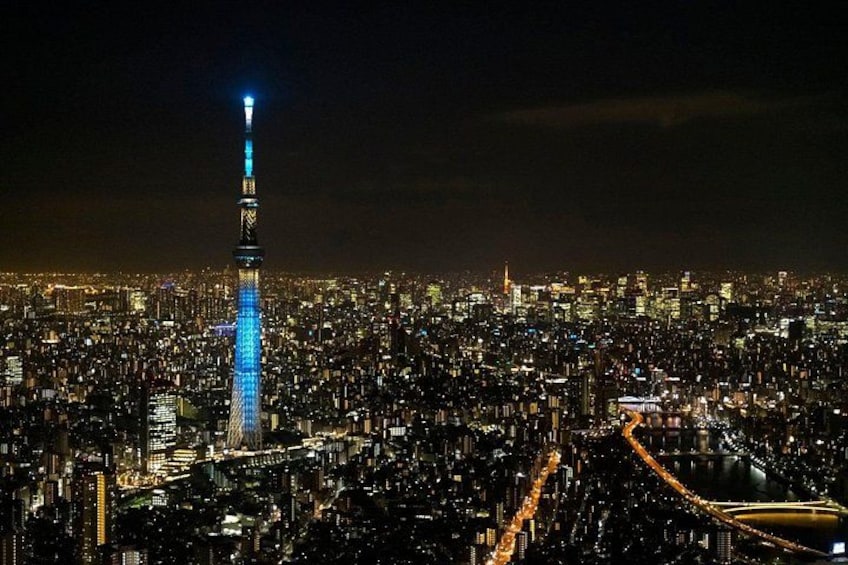 A cityscape at night with a prominent illuminated tower, dense urban buildings, and a river. 3