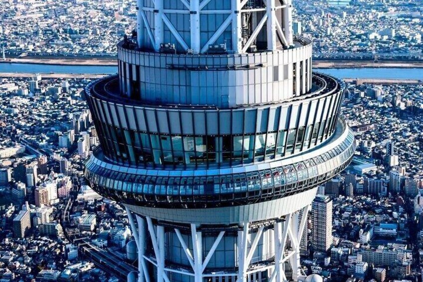 A tall, cylindrical skyscraper with a circular observation deck, surrounded by a dense urban cityscape. 1