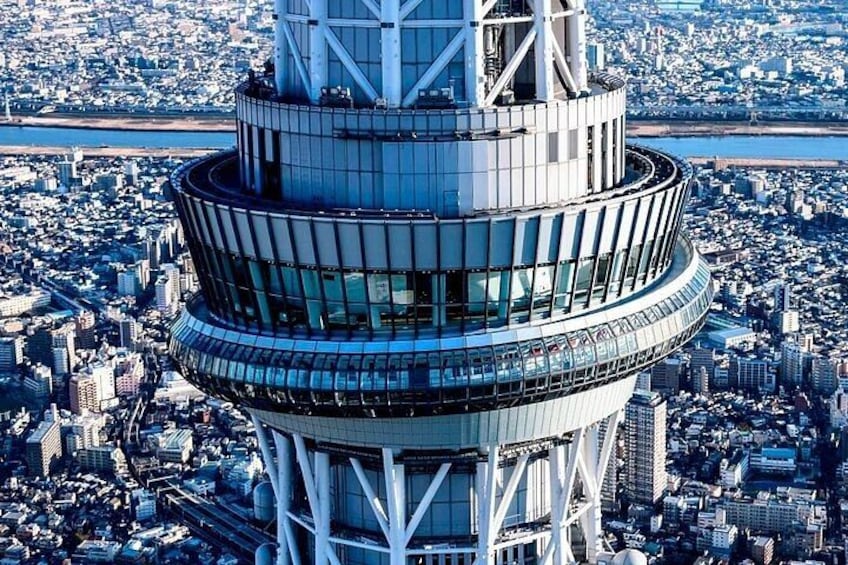 A tall, cylindrical skyscraper with a circular observation deck, surrounded by a dense urban cityscape. 2