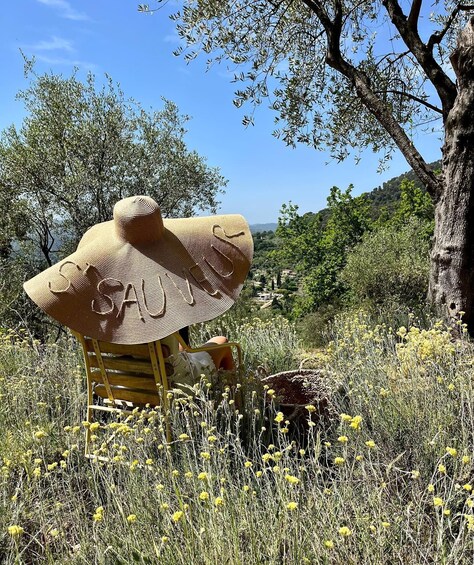 A straw hat sculpture in a field with yellow flowers and trees. 1