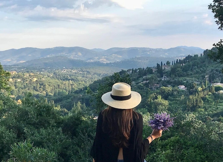 A person with a hat holding a bouquet, overlooking a mountainous landscape with scattered houses. 3