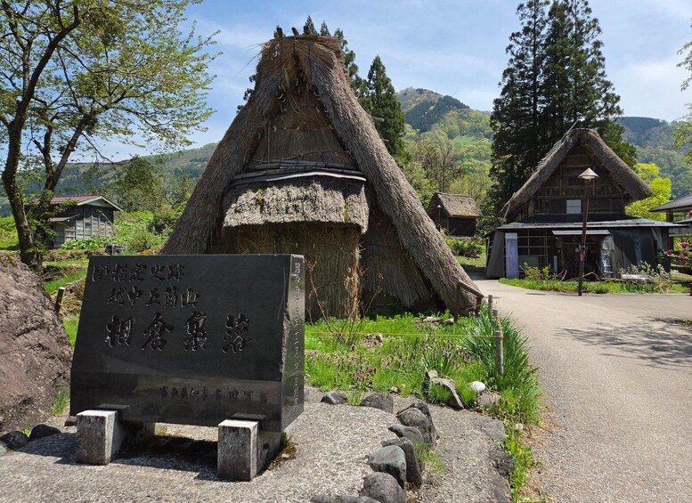A traditional thatched-roof hut, a stone monument with inscriptions, and a wooden building in a rural setting. 5