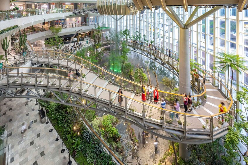 A multi-level shopping mall with glass railings, greenery, and people walking. 4