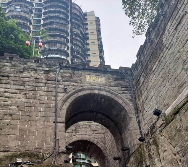 A stone archway with a plaque, surrounded by modern buildings and greenery. 1