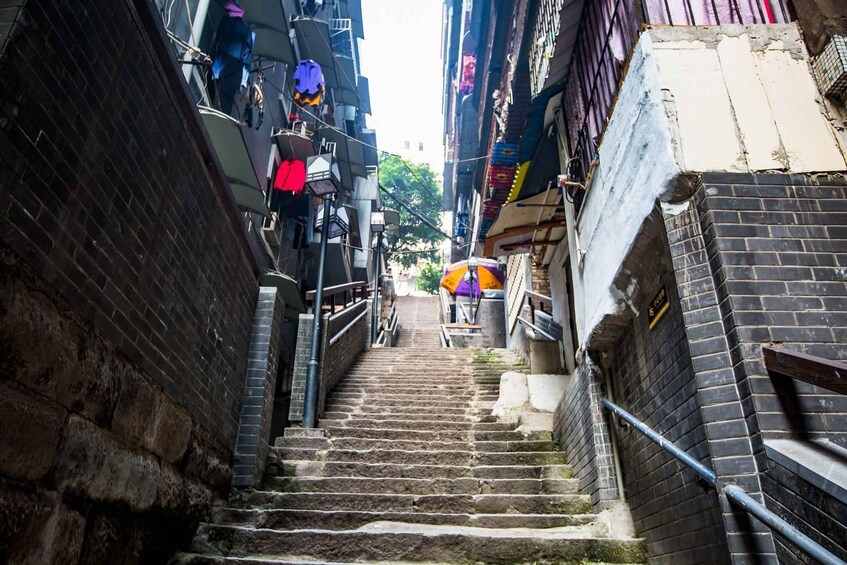 A narrow alley with brick walls, a metal staircase, and a colorful umbrella in the distance. 3