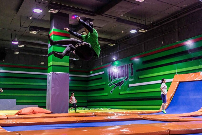An indoor trampoline park with green and orange padded areas and a person performing a trick. 2