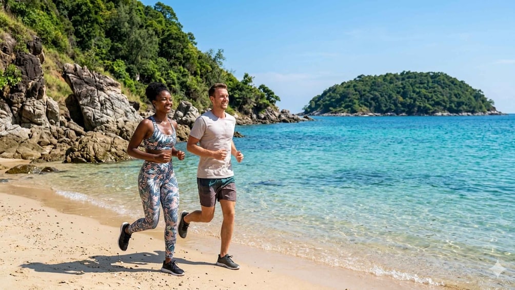 Two people jogging on a beach with clear water and a rocky coastline. 3