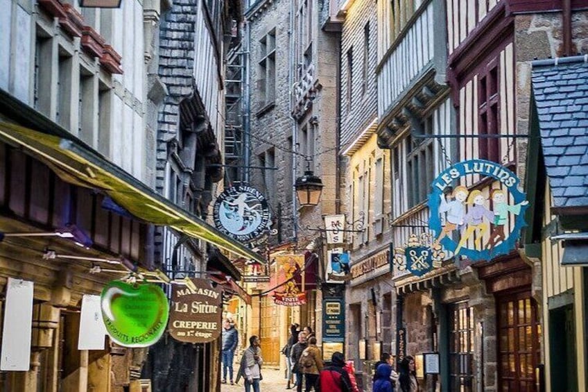 A narrow street with old buildings, a clock, and various shop signs. 3