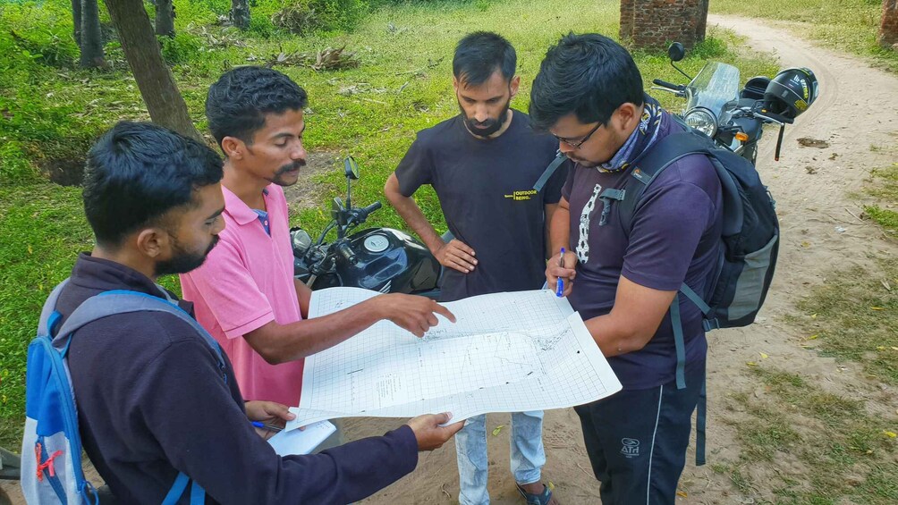 Four people examining a map outdoors with a motorcycle in the background. 4