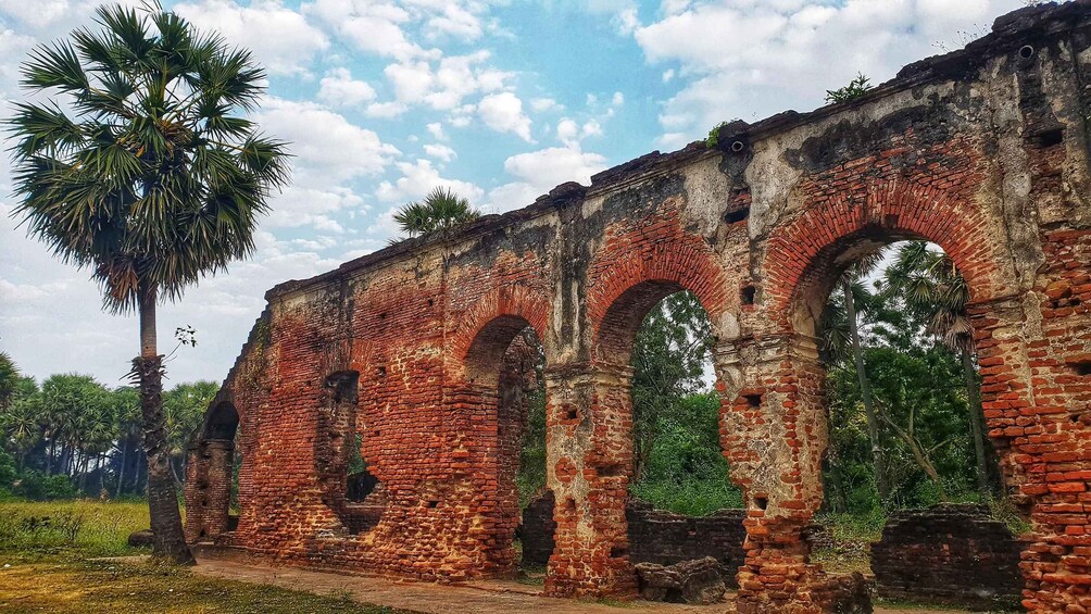An ancient brick structure with arches and a palm tree in the foreground. 1