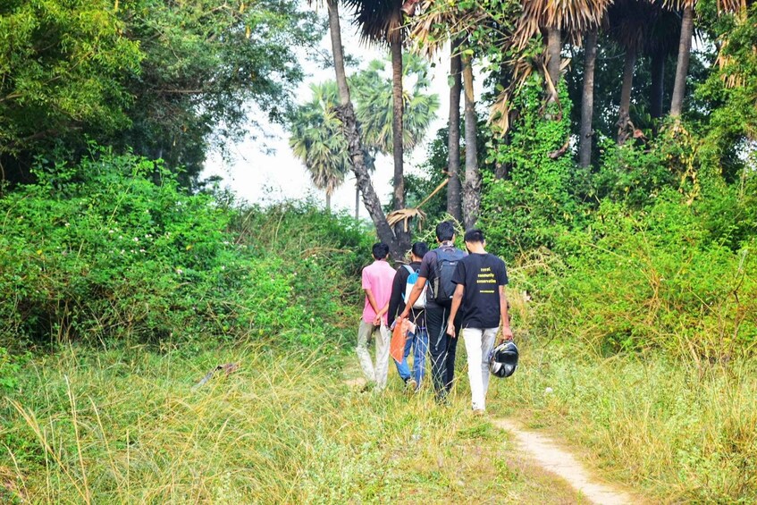 A group of people walking on a dirt path surrounded by dense greenery and tall trees. 3
