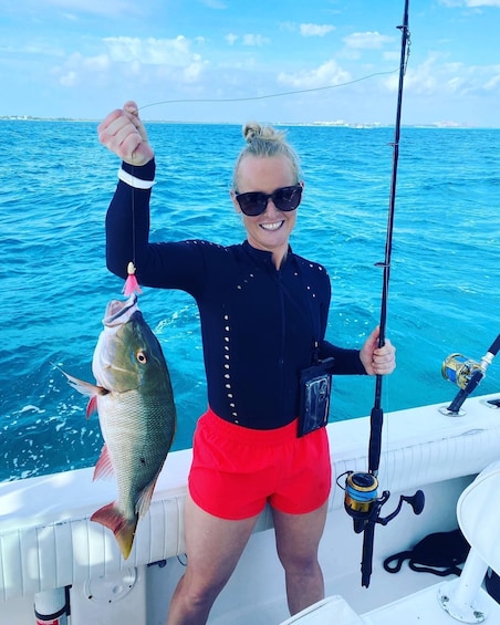 A person holding a fish on a boat with a fishing rod. 1