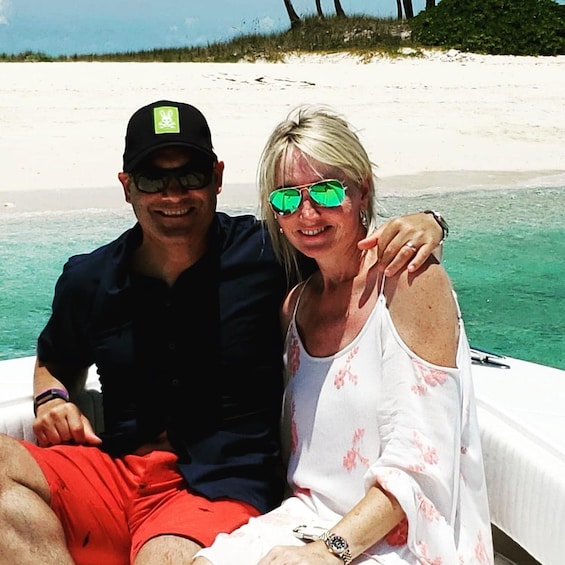 Two people on a boat near a sandy beach with clear water. 5