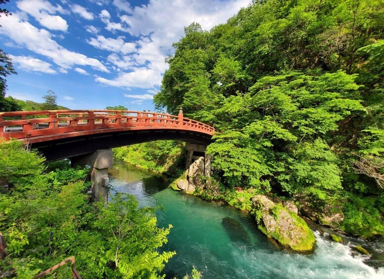 A red bridge over a clear river surrounded by lush greenery. 3