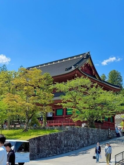 A traditional Japanese building with a tiled roof and red walls, surrounded by trees and a stone wall. 4