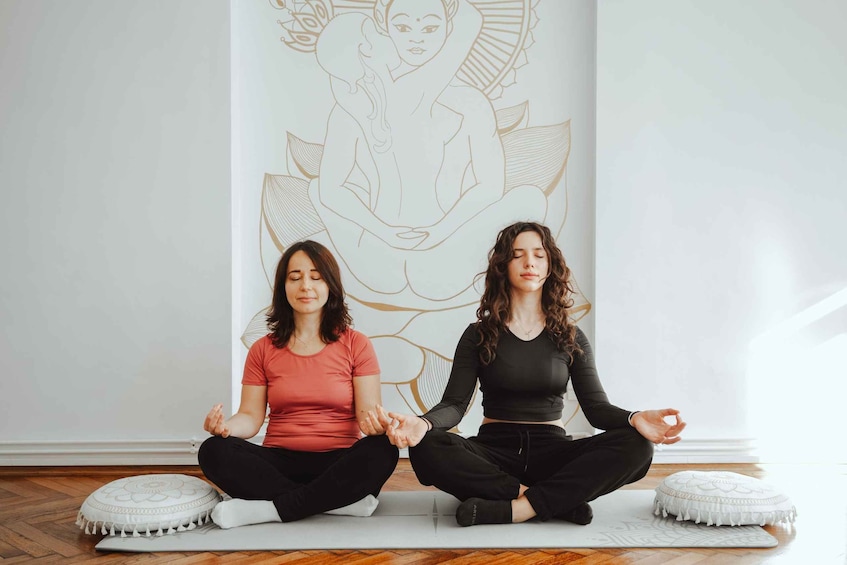 Two people meditating on yoga mats in front of a wall with a large drawing. 5