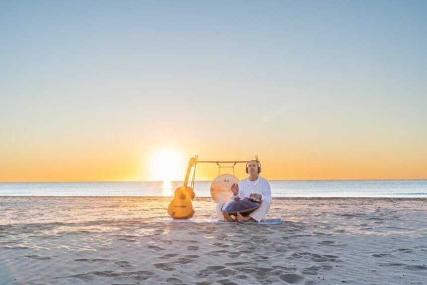 A person sitting on the beach with a guitar and a surfboard. 3
