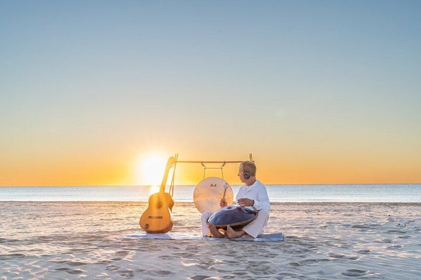 A person sitting on the beach with a guitar and a drum set. 4