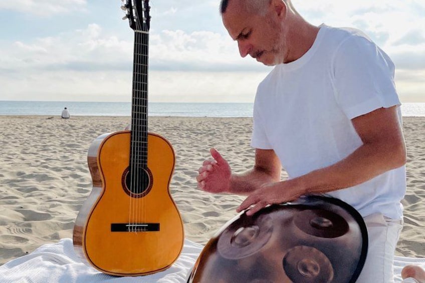 A person sitting on a beach with a guitar and a drum. 1