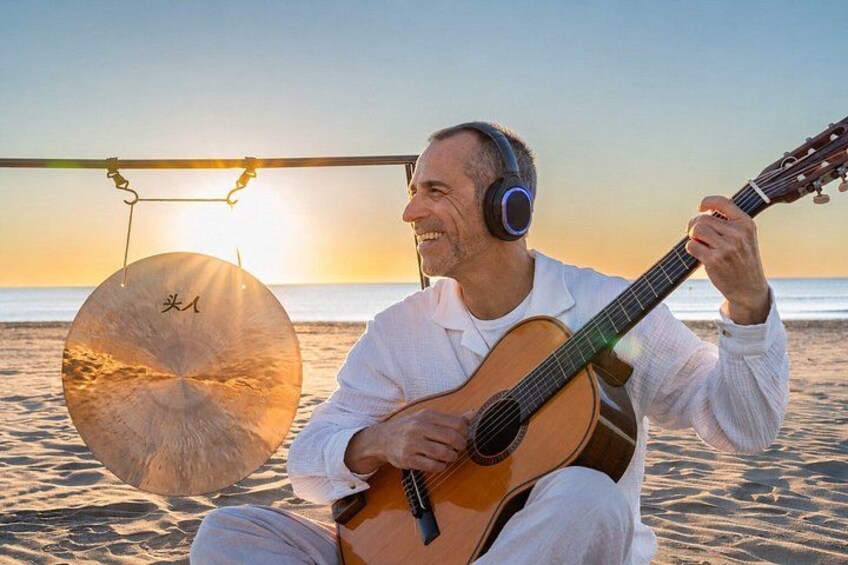 A person playing a guitar on a beach at sunset. 1