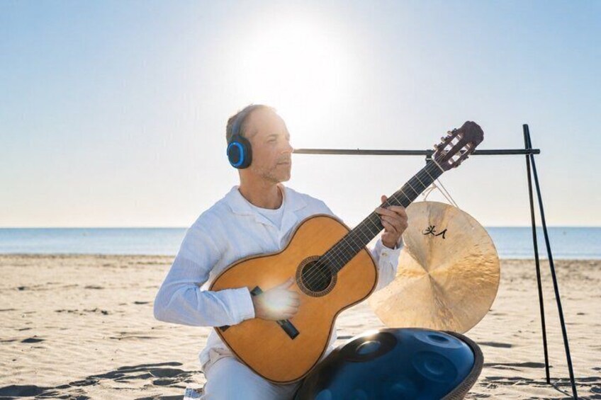 A person playing a guitar on a beach with a drum set and a microphone stand. 2