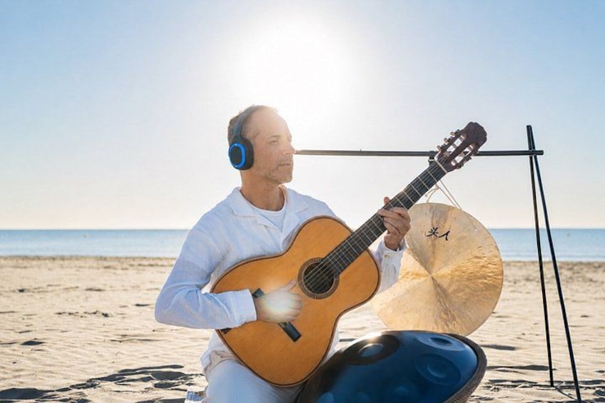 A person playing a guitar on a beach with a stand holding a tambourine. 2