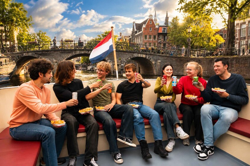 A group of people sitting on a bench by a canal, eating food and holding a flag. 3