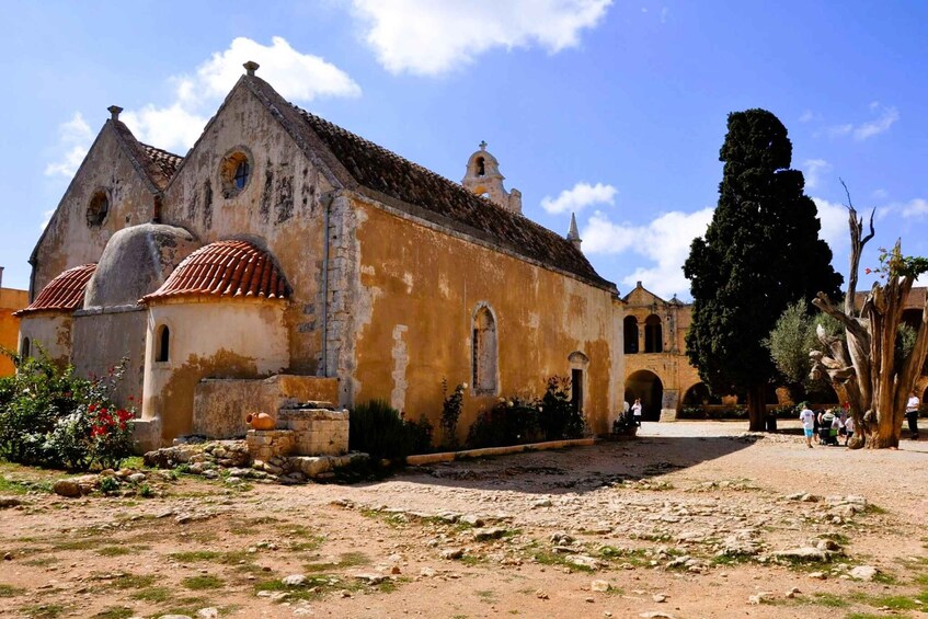 A historic church with a bell tower, surrounded by a courtyard with visitors and a large tree. 2