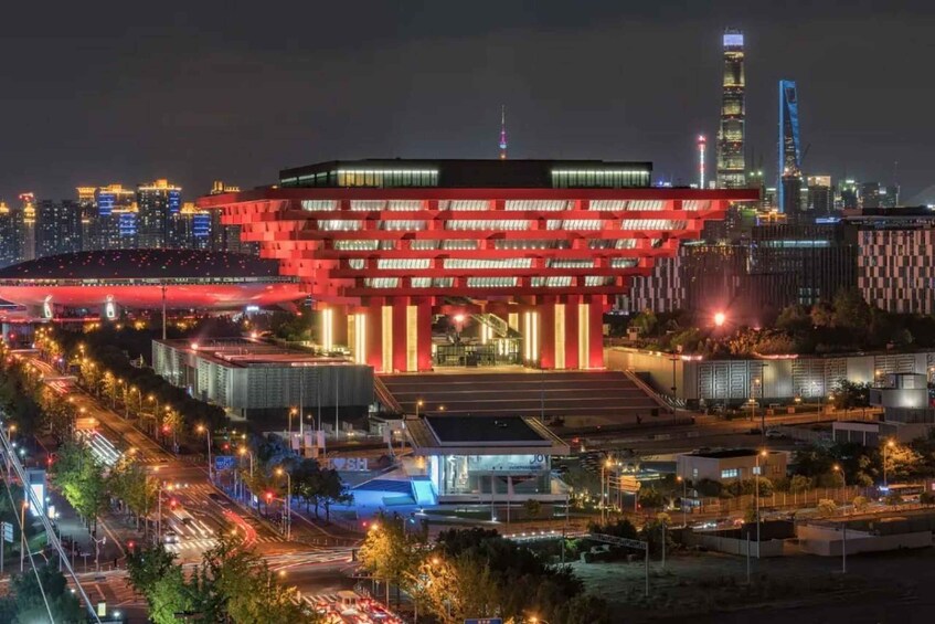 A modern building with red lighting, surrounded by a cityscape with tall buildings and a stadium. 3