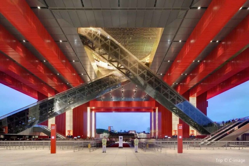 A modern architectural structure with a prominent red and gold color scheme, featuring a large, angular design element that resembles a bridge or arch. 1
