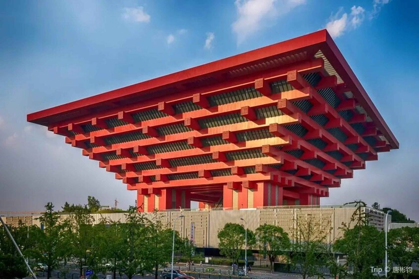 A modern red building with a unique geometric design, surrounded by trees and a clear sky. 4