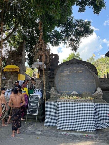 A stone monument with inscriptions, a checkered cloth, and a group of people in traditional attire. 4