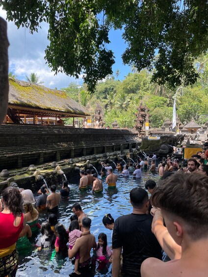 A group of people bathing in a natural pool surrounded by traditional architecture and lush greenery. 5