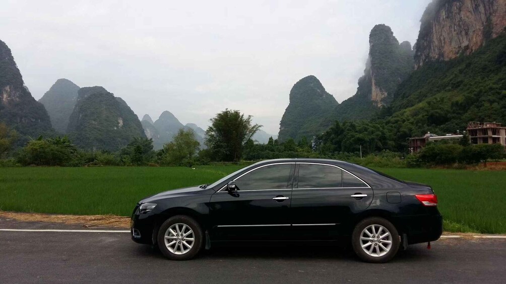 A black sedan parked on a road with a mountainous landscape in the background. 1