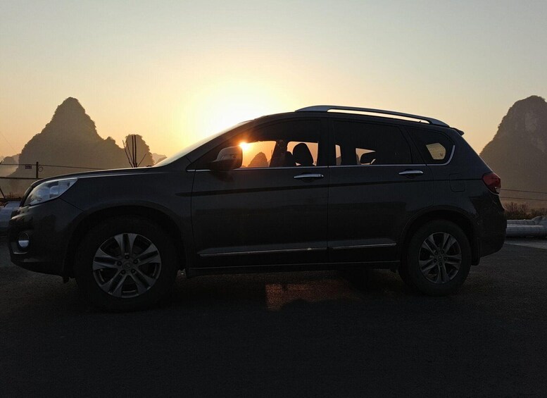 A dark-colored SUV parked on a road with a sunset in the background. 4