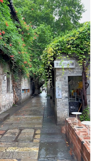 A narrow stone pathway flanked by lush greenery and a stone building with signage. 5