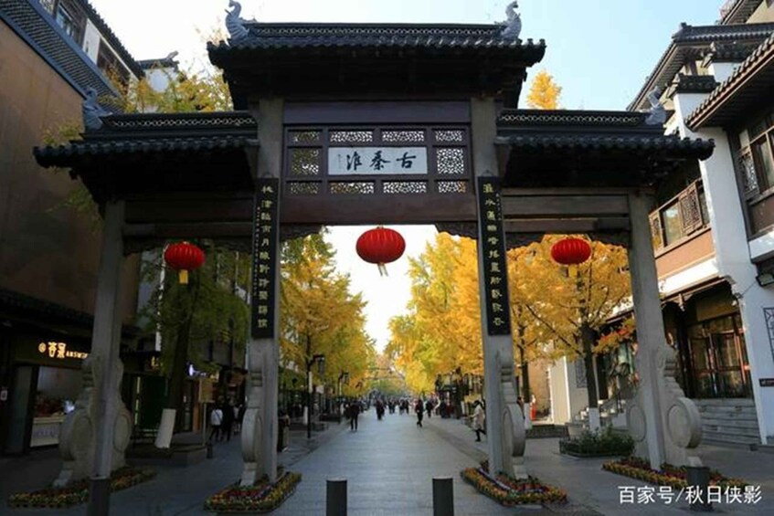 A traditional Chinese gate with red lanterns, surrounded by autumn-colored trees and buildings. 2