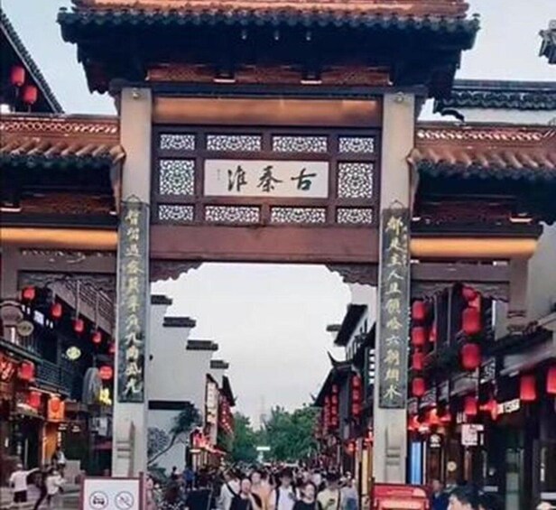 A traditional Chinese archway with intricate designs and red lanterns, leading into a bustling street with shops and pedestrians. 3