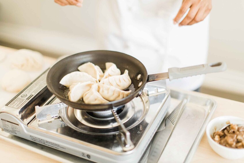 A person cooking dumplings in a pan on a stove. 3