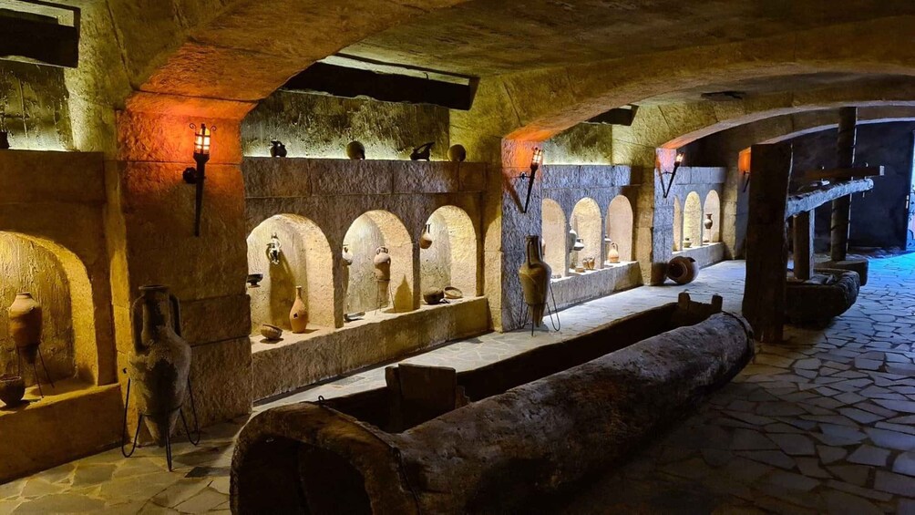 An ancient stone structure with arched niches displaying pottery and a long bench. 5